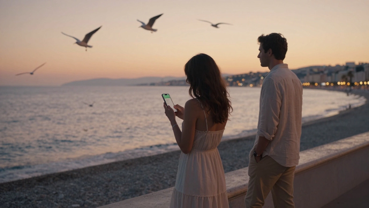 A man and woman strolling along a quiet Nice beach at sunset, the sea glowing behind them.